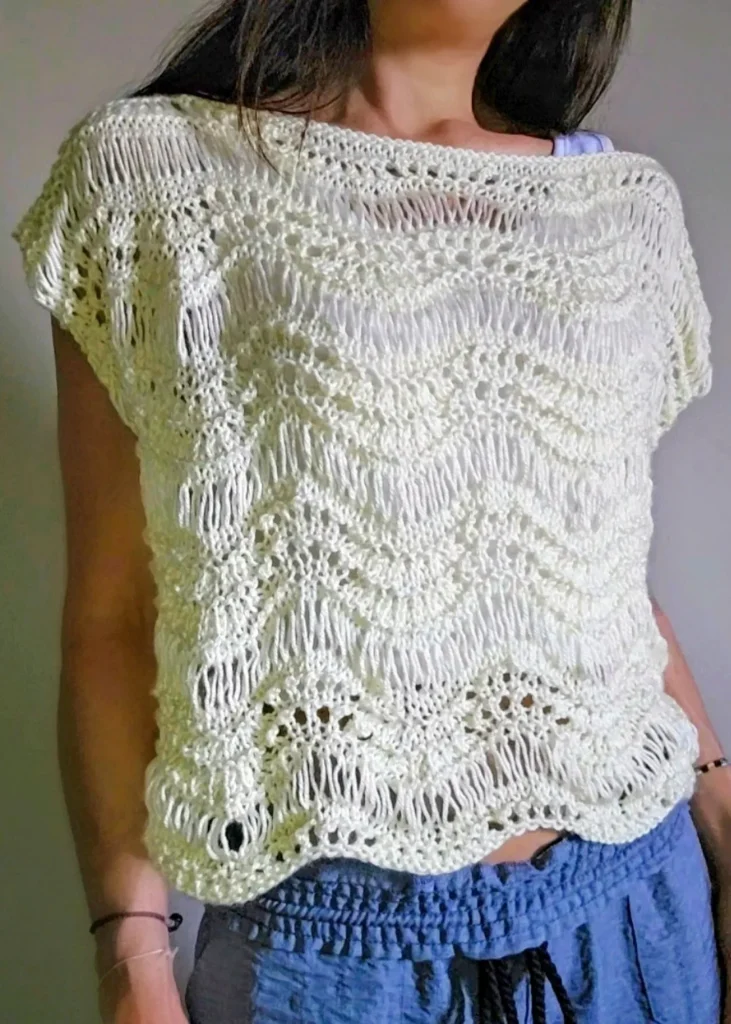 A person wearing a handmade knitted sweater in the color Ivory. It features a scalloped hem and a dropped stitch design.