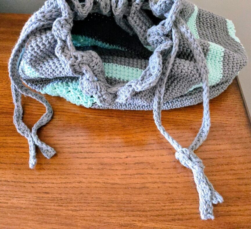The handmade crochet bag is opened and shows how to knot the ends of the drawstring.