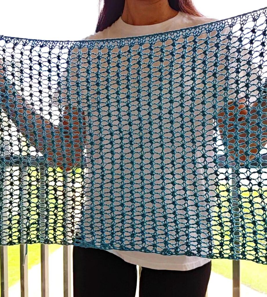 A woman holding up the Carefree Lacy Poncho showing the delicate stitch.