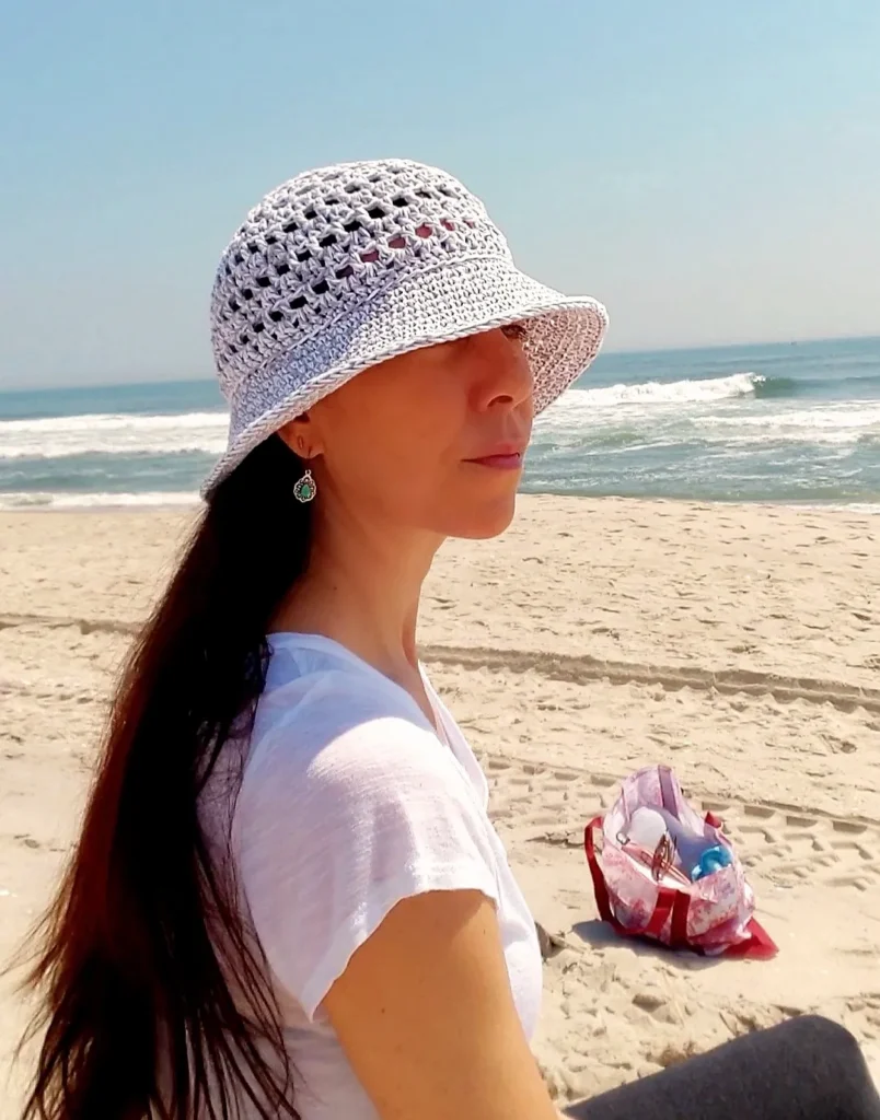 A wide brimmed crochet sun hat in a light colored cotton yarn, featuring an intricate open work pattern on the crown and a sturdy structured brim.
