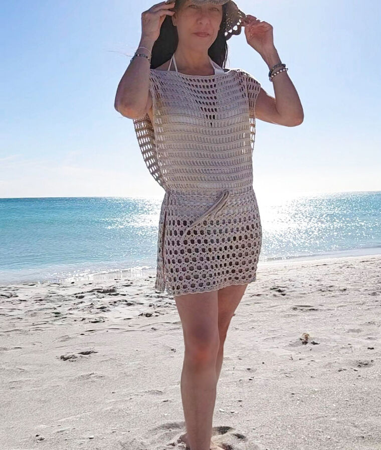 Woman wearing a beige crochet beach cover up dress on a sunny beach.