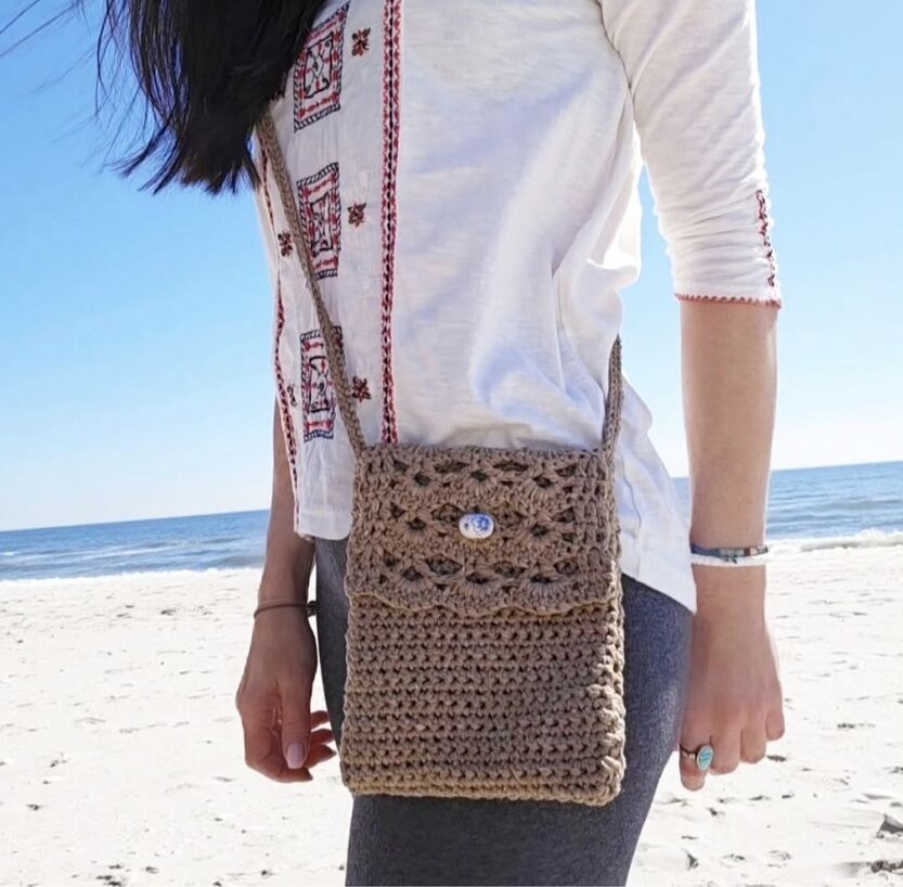 Free crochet pattern for an easy crossbody bag with a brown shell stitch flap on a beach.