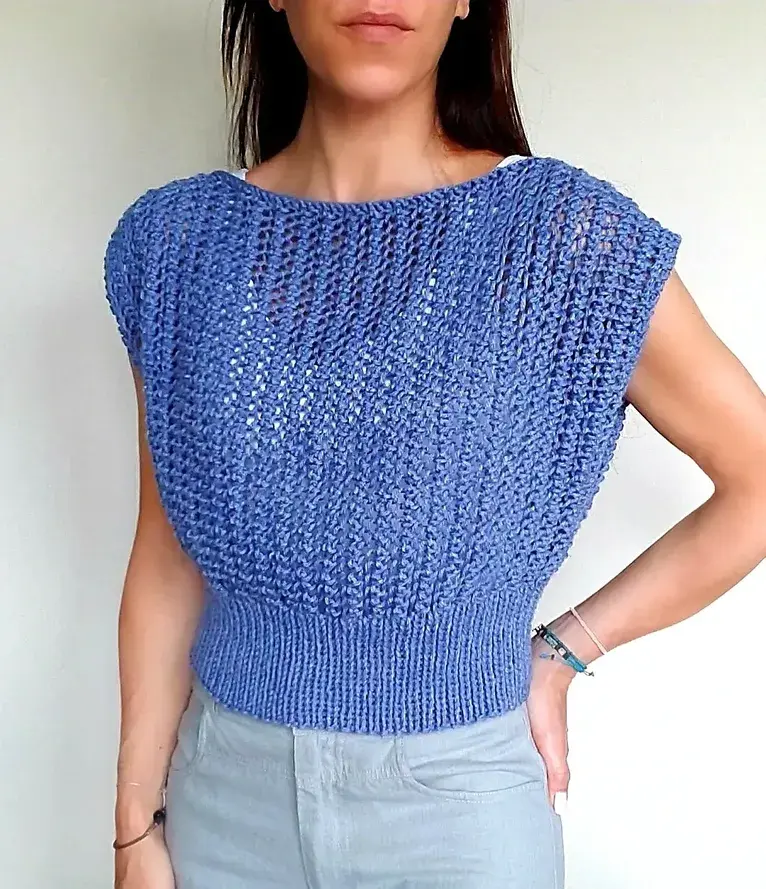 Woman wearing a blue, cropped lace stitch poncho sweater with a ribbed waist hem.