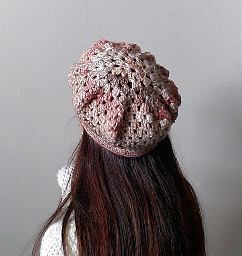 Rear view of a person wearing the Granny Crochet Beret, a textured slouchy hat handmade with pink and beige variegated yarn.