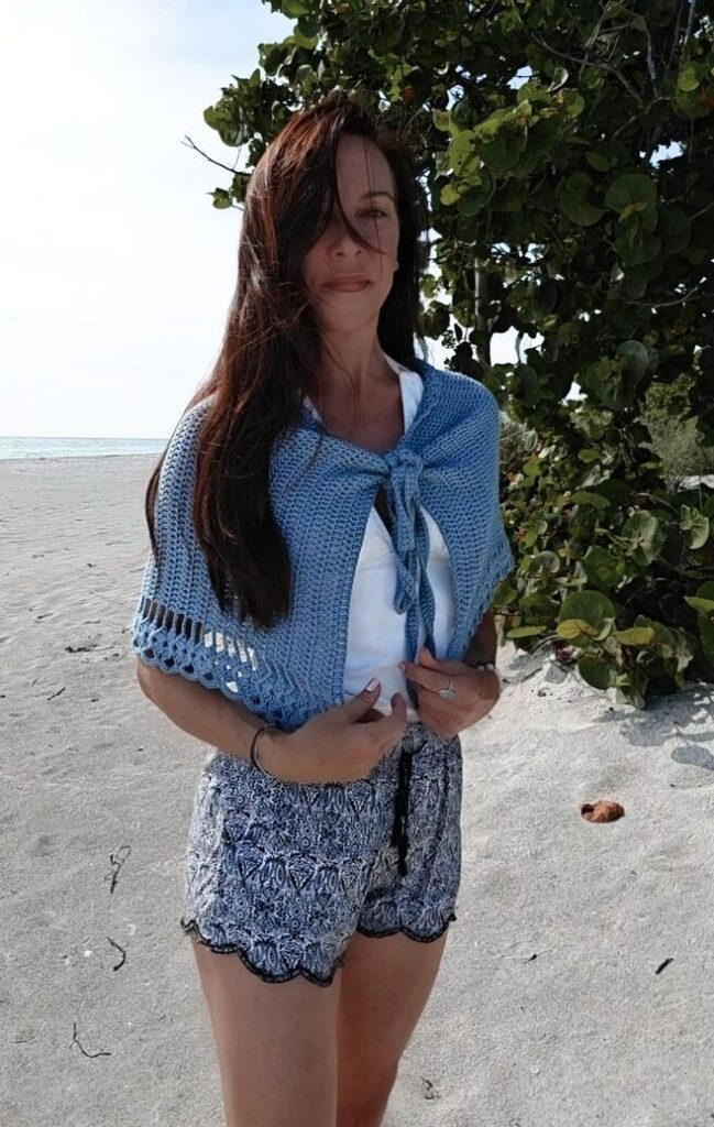 A woman wearing the crochet wrap skirt as a shawl on a sunny tropical beach.