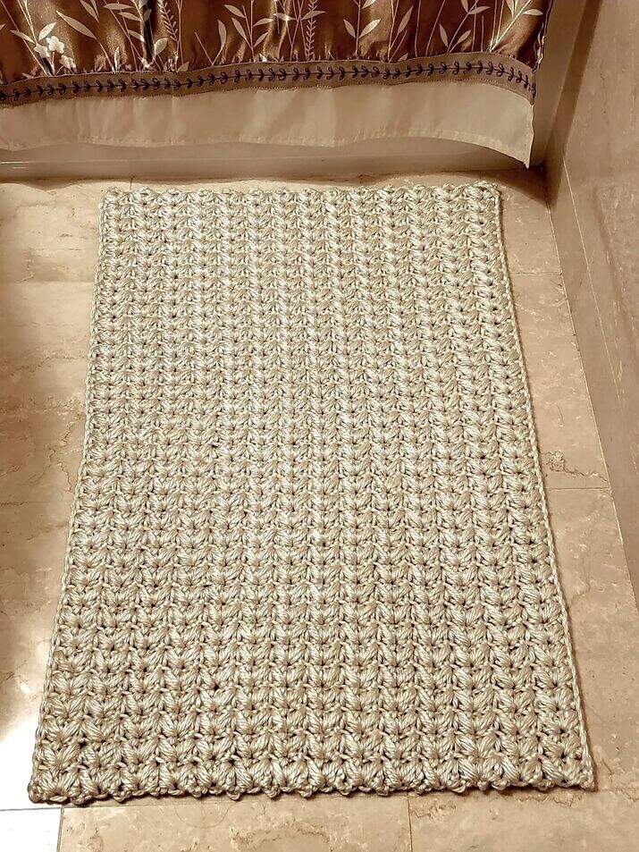 A textured cream crochet bath mat made with super bulky yarn, styled on a neutral tile bathroom floor.
