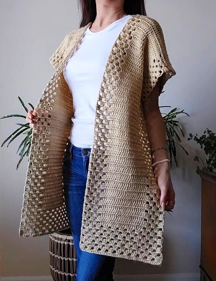 A model wearing a handmade beige crochet ruana featuring a distinct open weave granny square pattern along the borders.