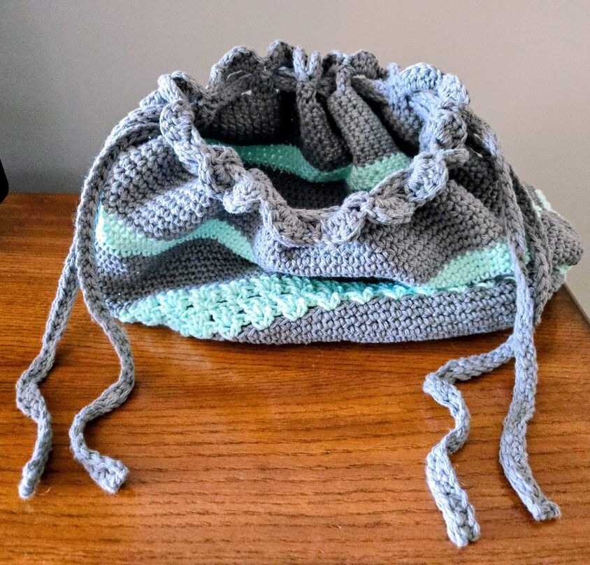 A guide on how to weave the drawstring at the top of the crochet bag.