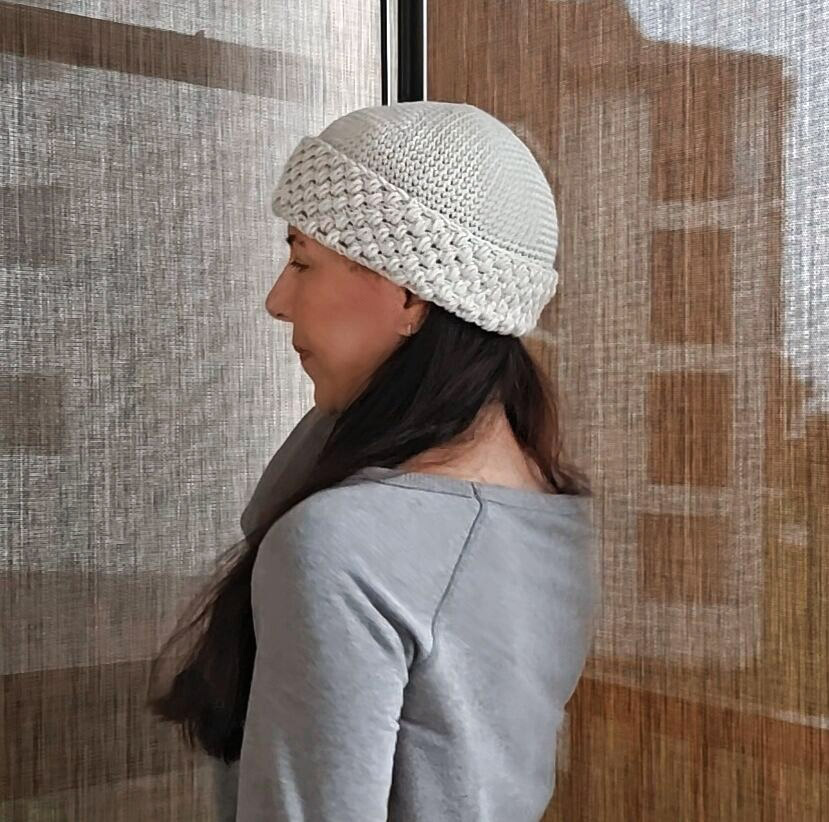 Woman wearing a grey beanie-style crochet hat with a thick puff stitch brim, viewed from the side profile.