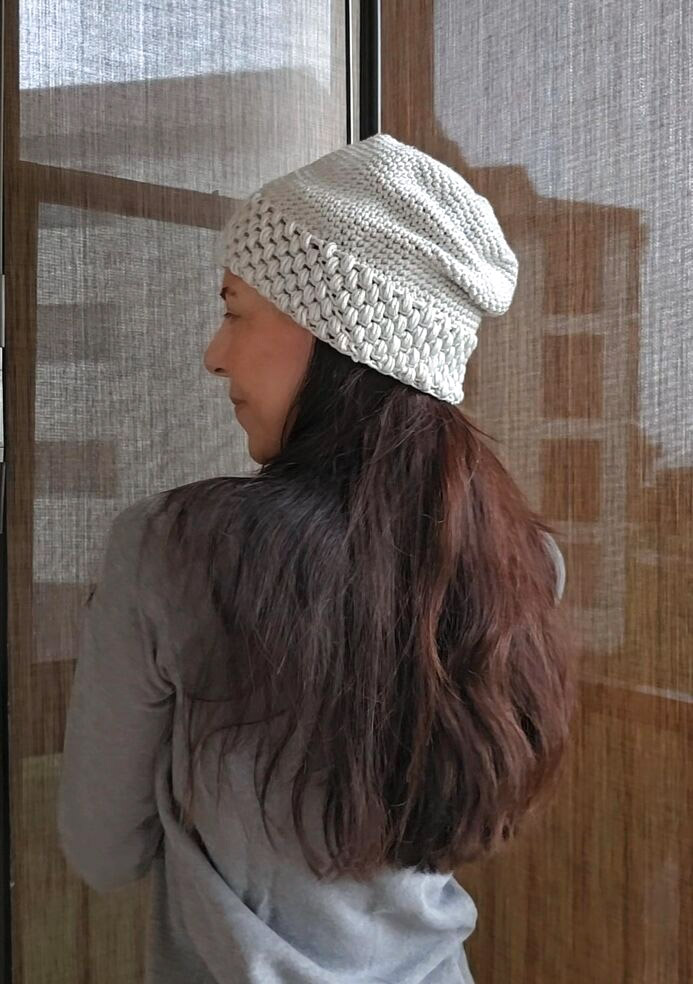 Woman with long brown hair wearing a light grey slouchy crochet beanie made with single crochets and a textured puff stitch band.